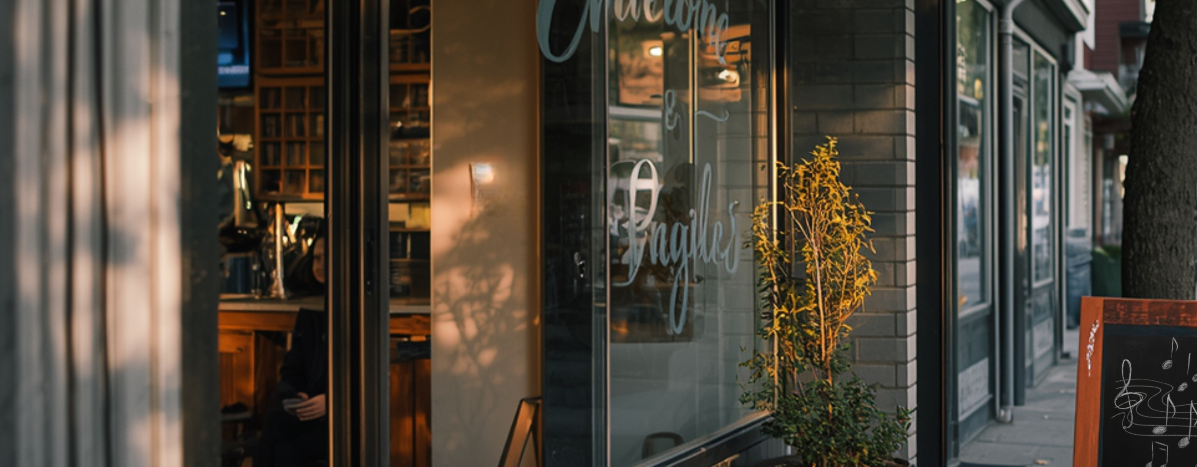 A small neighborhood tutoring center storefront in late afternoon. A glass door with soft-script lettering, warm light spilling onto the sidewalk, a wooden bench beside the door, autumn leaves on the path.